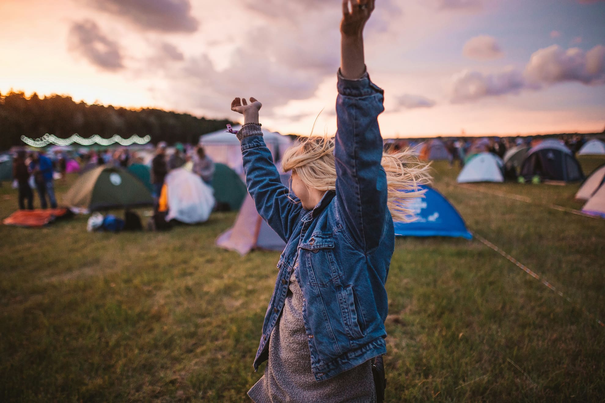 A woman raising her arms in the air in front of tents